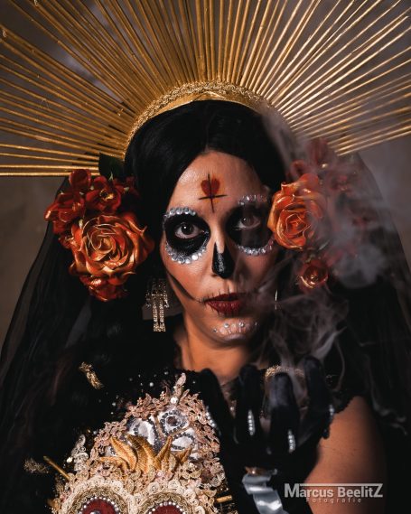 Frau mit traditionellem Totenkopf-Makeup, schwarzen Blumen und goldenen Strahlen.