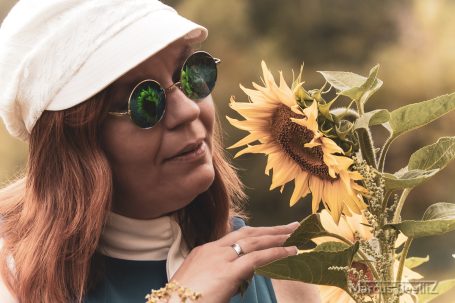 Frau mit Sonnenbrille bewundert eine Sonnenblume im Freien.