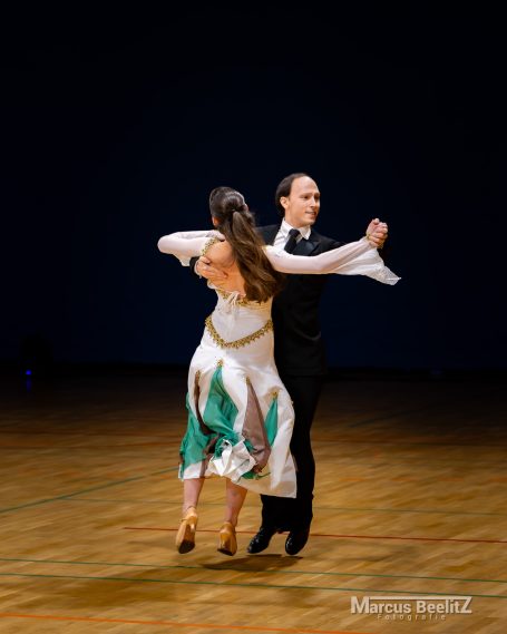 Tanzpaar in eleganter Pose, Frauenkleid mit Grüntönen, männlicher Partner in schwarzem Anzug.