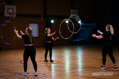 Drei Frauen üben mit Hula-Hoop-Reifen in einer Sporthalle.