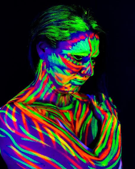 Eine Frau mit neongrüner und -roter Körperbemalung auf schwarzem Hintergrund.
