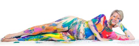 Frau liegt auf dem Boden, bunt bemalt mit verschiedenen Farben.