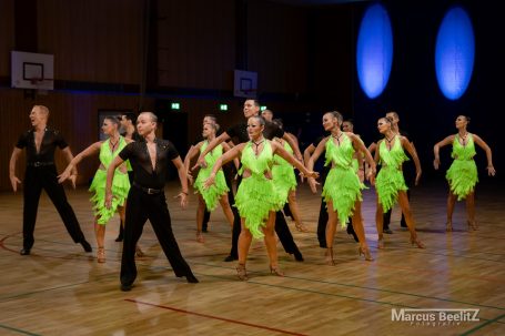 Tanzgruppe in leuchtend grünen Kostümen, dynamische Bewegungen in einer Sporthalle.