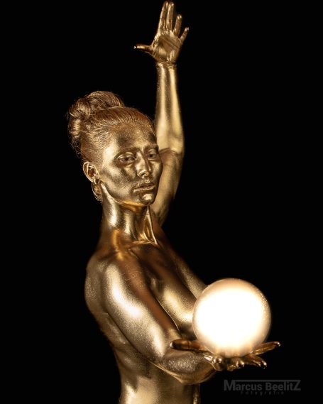 Eine goldene Frau, die eine leuchtende Kugel hält und eine Hand hebt.