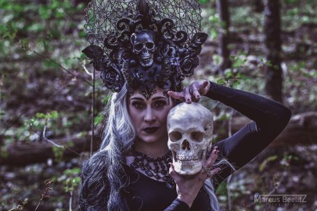 Frau mit schwarzer Kopfbedeckung und Totenschädel in einem Wald.