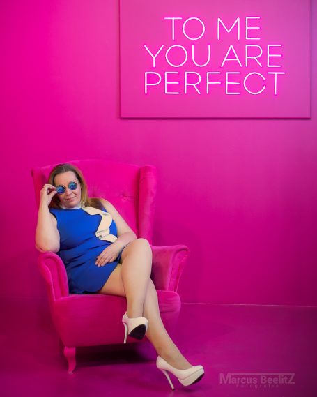 Frau mit Sonnenbrille in blauer Kleidung sitzt entspannt auf einem pinken Sessel.