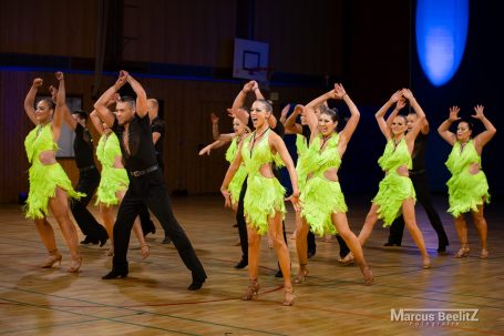 Tanzgruppe in leuchtend grünen Kostümen zeigt eine Choreografie auf der Bühne.