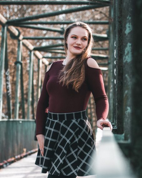 Junge Frau in einem schulterfreien Oberteil und kariertem Rock, steht auf einer Brücke.