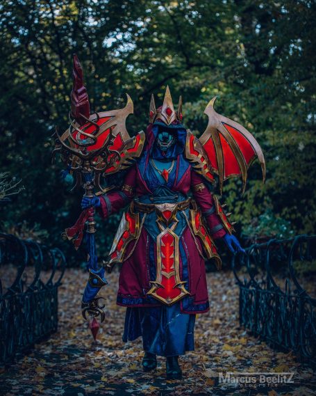 Eine festlich gekleidete Person in Fantasy-Rüstung mit einem Stab in einem Wald.