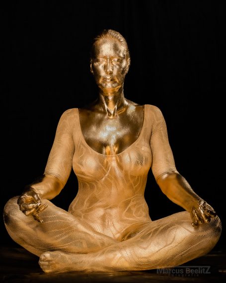 Sitzende Frau in meditativer Pose, goldfarben mit sanften Linien und Schatten.